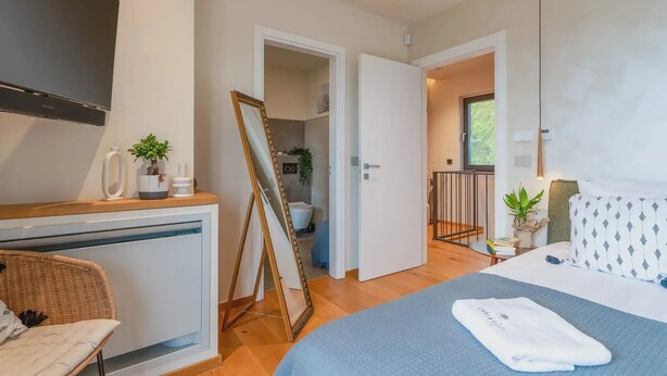 Una habitació d'hotel moderna amb un llit, una taula de treball, una televisió i un bany visible a través d'una porta oberta.