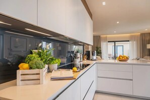 A modern kitchen with white cabinetry, a black countertop, and a built-in stove. There are plants, a bowl of fruit, and a coffee maker on the counter. - Christall in Kastelir (Kastelir-Labinci)