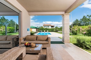 A covered outdoor seating area with wicker furniture, a pool in the background, and a view of a house across the street. - Fantasia in Barban With 4 Bedrooms and 2 Bathrooms (Marcana)
