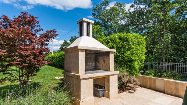 A stone-built outdoor kitchen with a chimney, surrounded by greenery and a paved patio. - Fantasia in Barban With 4 Bedrooms and 2 Bathrooms (Marcana)