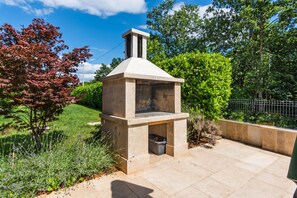 A stone-built outdoor kitchen with a chimney, surrounded by greenery and a paved patio. - Fantasia in Barban With 4 Bedrooms and 2 Bathrooms (Marcana)