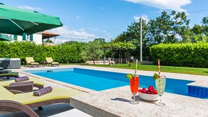 A poolside area with lounge chairs, a table with drinks, and a green umbrella. - Fantasia in Barban With 4 Bedrooms and 2 Bathrooms (Marcana)