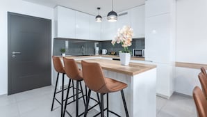 A modern kitchen with white cabinets, a wooden countertop, and two bar stools. - Twins III in Crikvenica (Crikvenica)