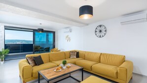 A modern living room with a yellow sofa, a wooden coffee table, and a view through large windows. - Twins III in Crikvenica (Crikvenica)