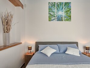 Een slaapkamer met een bed, twee nachtkastjes, een wanddecoratie en een vaas met gedroogde planten.