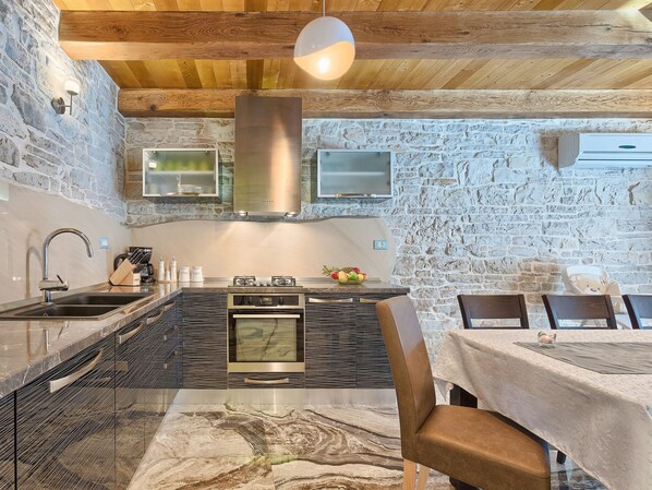 Een keuken met een stenen muur, houten plafond, roestvrijstalen apparatuur en een eethoek met een tafel en stoelen.