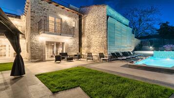 A stone building with a pool, outdoor seating, and a well-lit entrance.