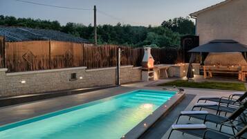 A swimming pool with lounge chairs, a barbecue area, and a stone wall.