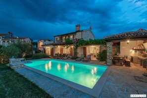 A swimming pool with lounge chairs, a patio area with a table and chairs, and a stone building with a tiled roof. - Bella Vista in Barat (Visnjan)