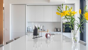 A modern kitchen with white cabinets, a central island with a glass top, and a vase with yellow flowers. - Loft Hvar in Hvar With 3 Bedrooms and 1 Bathrooms (Hvar)