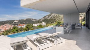 A modern outdoor pool area with lounge chairs, a dining set, and a view of a town and hills in the background. - Loft Hvar in Hvar With 3 Bedrooms and 1 Bathrooms (Hvar)