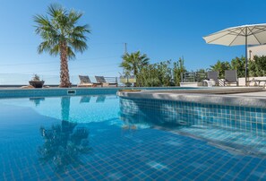 Una piscina azul cristalina con bordes de azulejos, rodeada de tumbonas y una palmera.