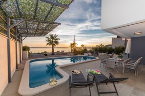 Una piscina en la azotea con sillones de descanso y una mesa, con vistas a una puesta de sol.