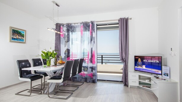 Una sala de estar moderna con comedor, televisor y balcón con cortinas.