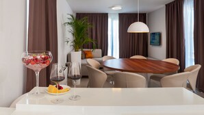 A modern dining area with a round wooden table, white chairs, and a white countertop. There is a potted plant and a sofa in the background. - More in Okrug Gornji (Okrug)