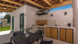 Uma área de cozinha externa com uma mesa, cadeiras, pia e armários de madeira.