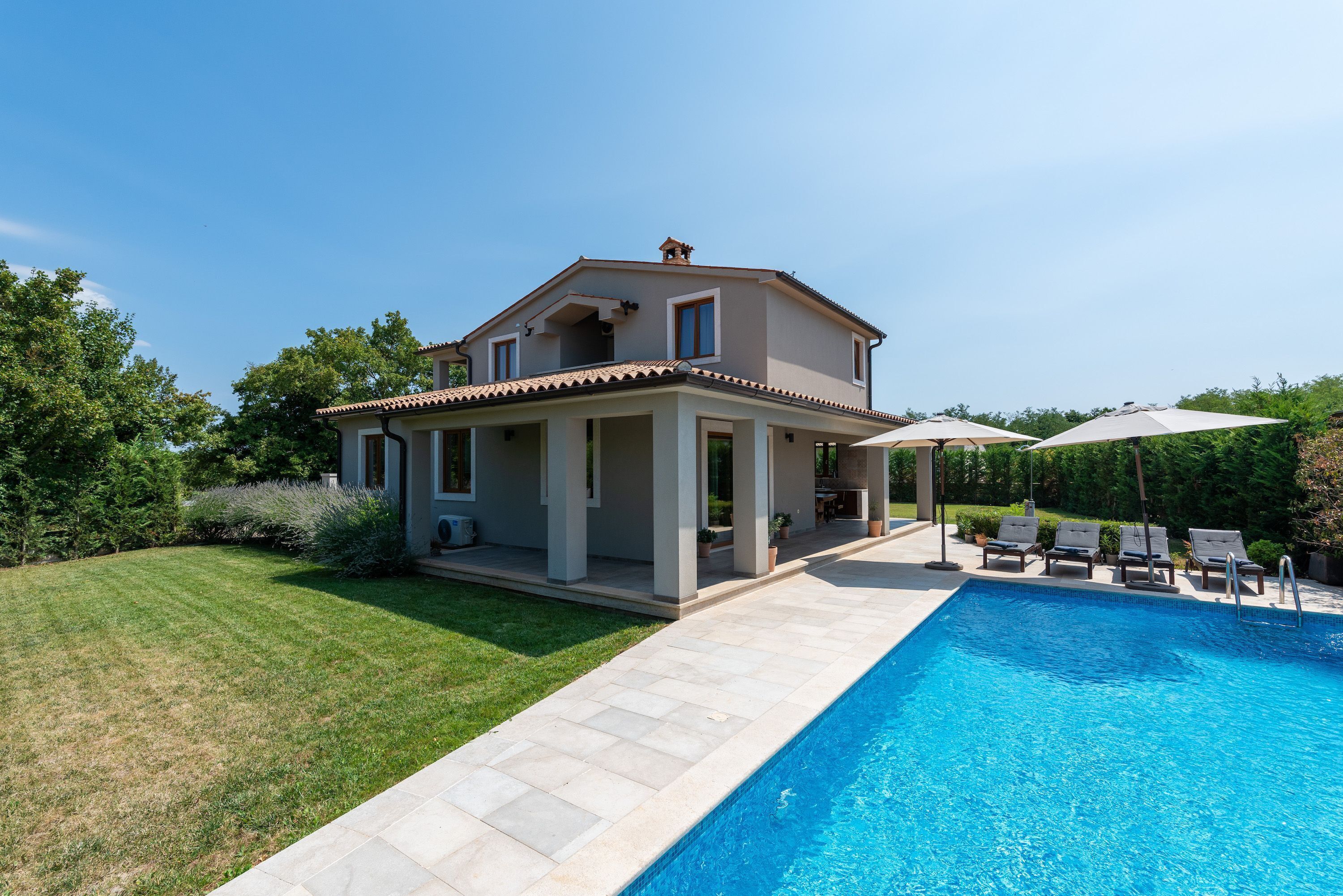 A two-story house with a swimming pool, a covered patio, and a well-maintained lawn.