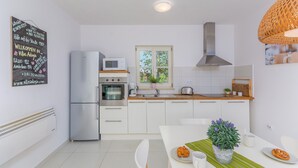 A modern kitchen with white cabinets, stainless steel appliances, and a window with a view of greenery. - Seconda in Rojni i With 3 Bedrooms and 3 Bathrooms (Barban)
