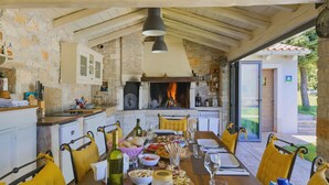 A rustic kitchen with stone walls, a fireplace, and a dining area with yellow chairs and a wooden table set for a meal. - Lipa in Krnica With 4 Bedrooms and 3 Bathrooms (Marcana)