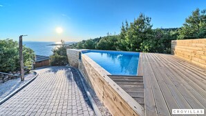 Une piscine dotée d’une terrasse en bois, entourée de verdure et offrant une vue sur la mer.
