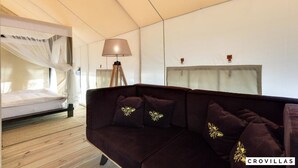 Une pièce comprenant un lit, un canapé brun foncé agrémenté de coussins décoratifs, une lampe sur pied et un grand miroir au mur.