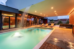 A modern outdoor pool area with a glass-enclosed lounge, a brick wall, and a wooden deck. - Grande Arche in Li Njan (Liznjan)