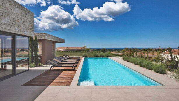 A modern pool area with a clear view of the ocean, lounge chairs, and a stone building. - Vigneto in Brtonigla (Brtonigla)