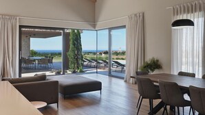 A spacious room with a large sliding glass door leading to a balcony with a view of the sea. There is a dining area with a table and chairs, and a seating area with a sofa and ottoman. - Vigneto in Brtonigla (Brtonigla)