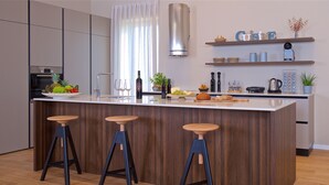 A modern kitchen with a central island, bar stools, a stainless steel range hood, and various kitchen appliances. - Vigneto in Brtonigla (Brtonigla)