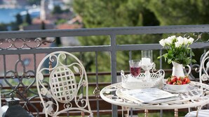 Un balcón con una mesa redonda dispuesta con una jarrón blanco, un vaso de bebida roja, un cuenco de fresas y un florero con flores blancas.