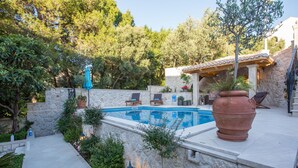 Una piscina rodeada de muros de piedra, con mobiliario exterior y una pérgola.