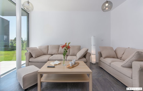 Una sala de estar moderna con un sofá color beige, una mesa de centro de madera y un florero con flores.