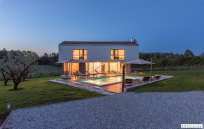 Una casa moderna de dos pisos con piscina, mobiliario exterior y un césped bien cuidado.