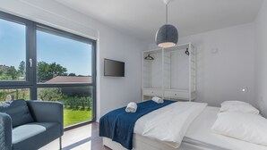 A modern bedroom with a large window, a bed with white linens, a grey sofa, and a hanging light fixture. - Complex Teca in Go an Draguzeti (Barban)