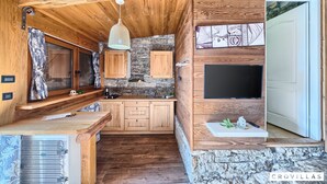A rustic kitchen with wooden cabinets, a stone wall, and a built-in TV. - Stone in Murter With 1 Bedrooms and 1 Bathrooms (Tisno)