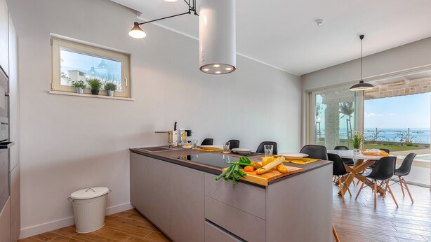 A modern kitchen with a central island, a dining area with a view, and a large window. - Natura III in Veprinac (Opatija)