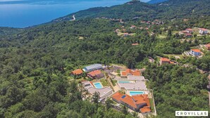 An aerial view of a residential area with houses, a swimming pool, and a road leading to the sea. - Natura III in Veprinac (Opatija)
