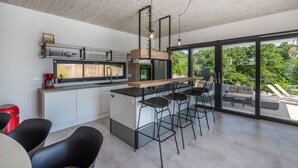 A modern kitchen with a bar area, large windows, and a view of the outdoors. - Grande Barbara in Vi Inada (Vizinada)