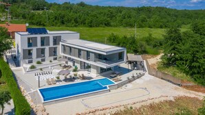A modern two-story house with a swimming pool, outdoor seating, and a view of a forested area. - Grande Barbara in Vi Inada (Vizinada)