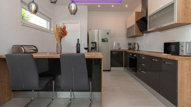 A modern kitchen with a central island, black chairs, stainless steel appliances, and pendant lighting. - Sun Stone in Trogir With 4 Bedrooms and 4 Bathrooms (Trogir)