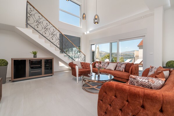 A spacious living area with a staircase, large windows, and a modern sofa set.