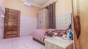 Un dormitorio con una cama, un armario de madera, una mesita de noche con un planchado y un ventilador de techo.