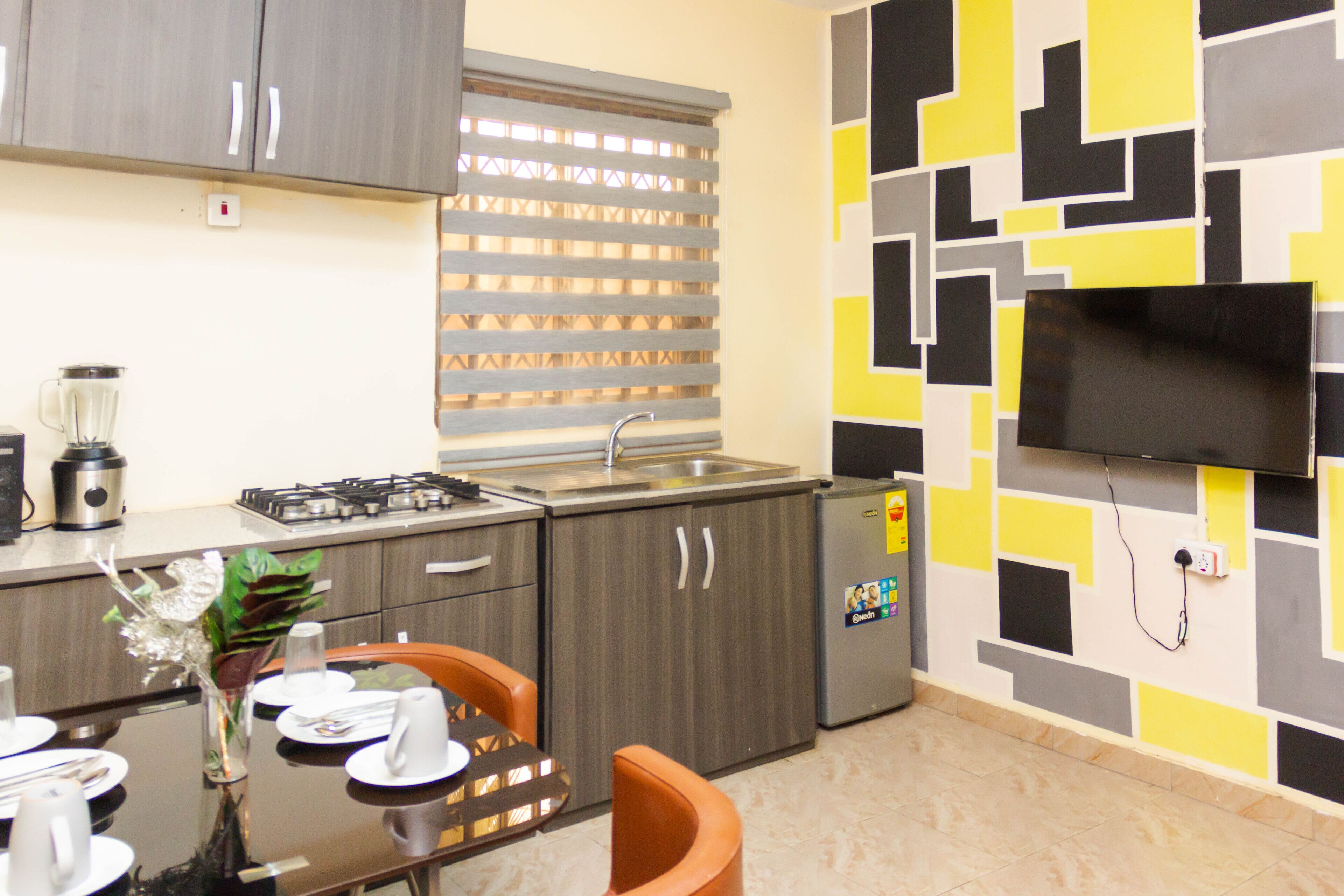 Una cocina moderna con armarios grises, estufa integrada, refrigerador y televisor de pantalla plana montado en la pared.