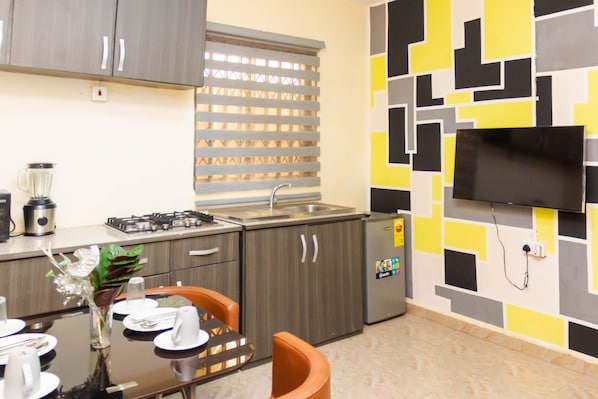 Una cocina moderna con armarios grises, estufa integrada, refrigerador y televisor de pantalla plana montado en la pared.
