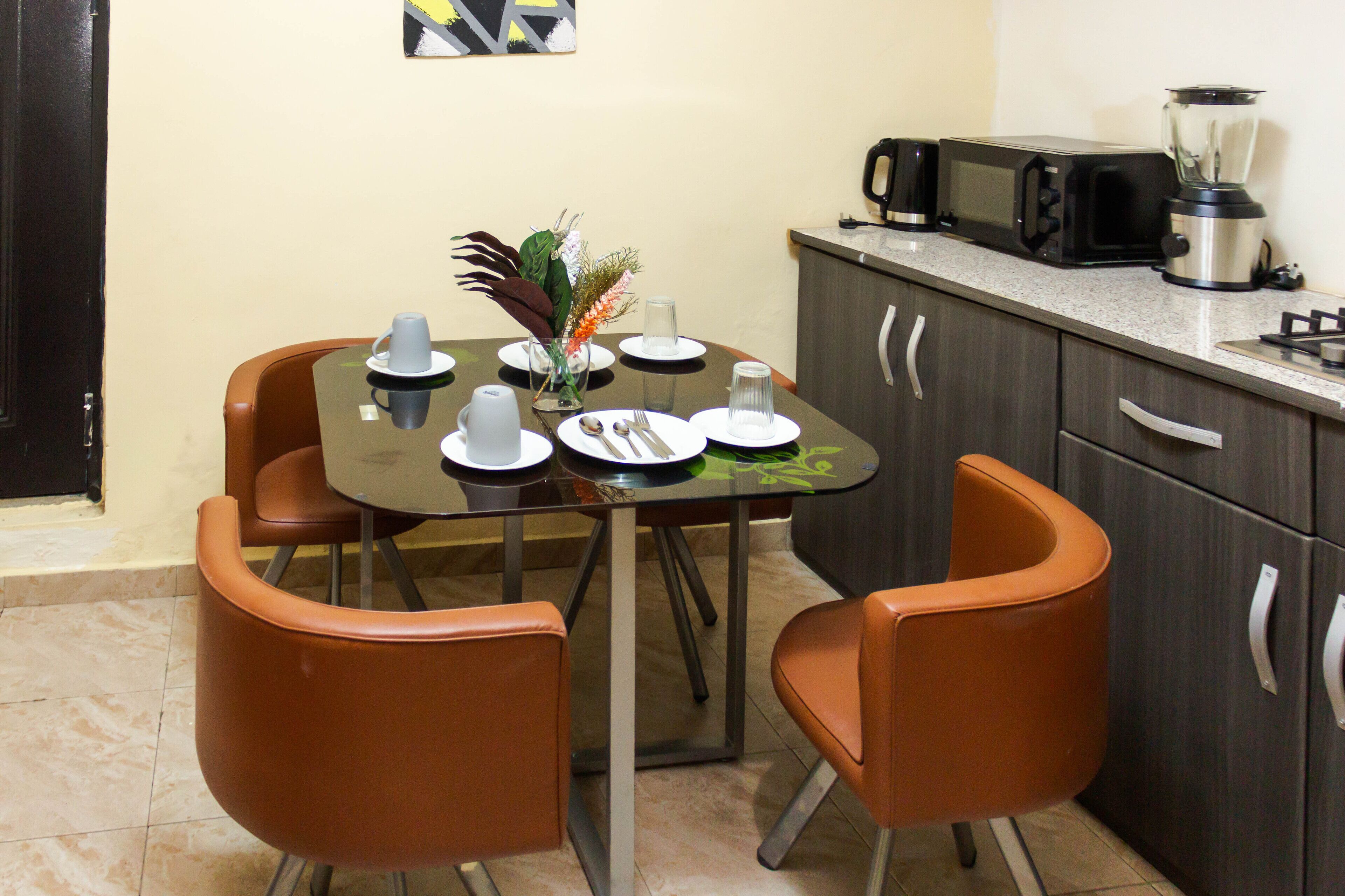 A compact kitchen with a dining table, four chairs, a microwave, a blender, and a cabinet.