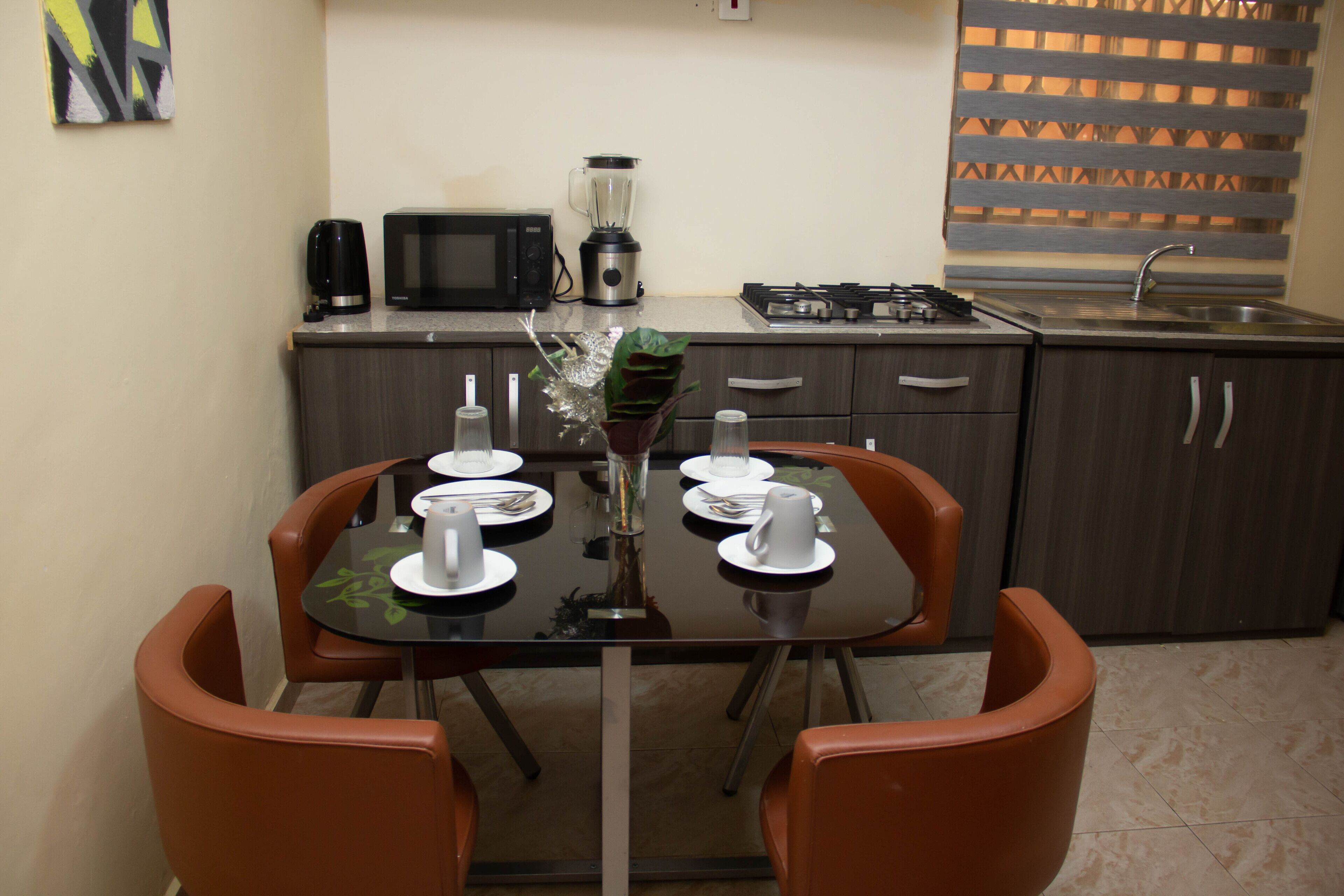 Cocina compacta con una mesa de comedor preparada para cuatro personas, microondas, licuadora y estufa a gas.