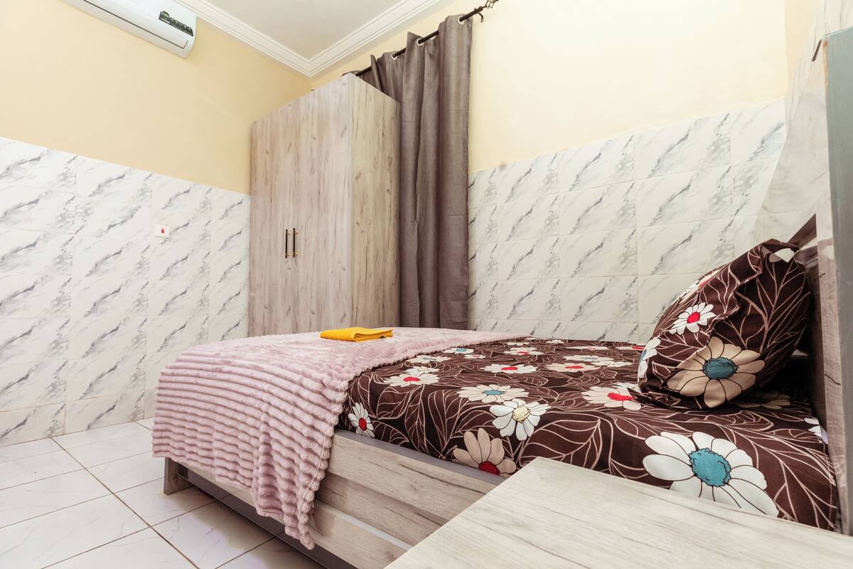 A bedroom with a bed, a wooden wardrobe, a curtain, and a marble-patterned wall.