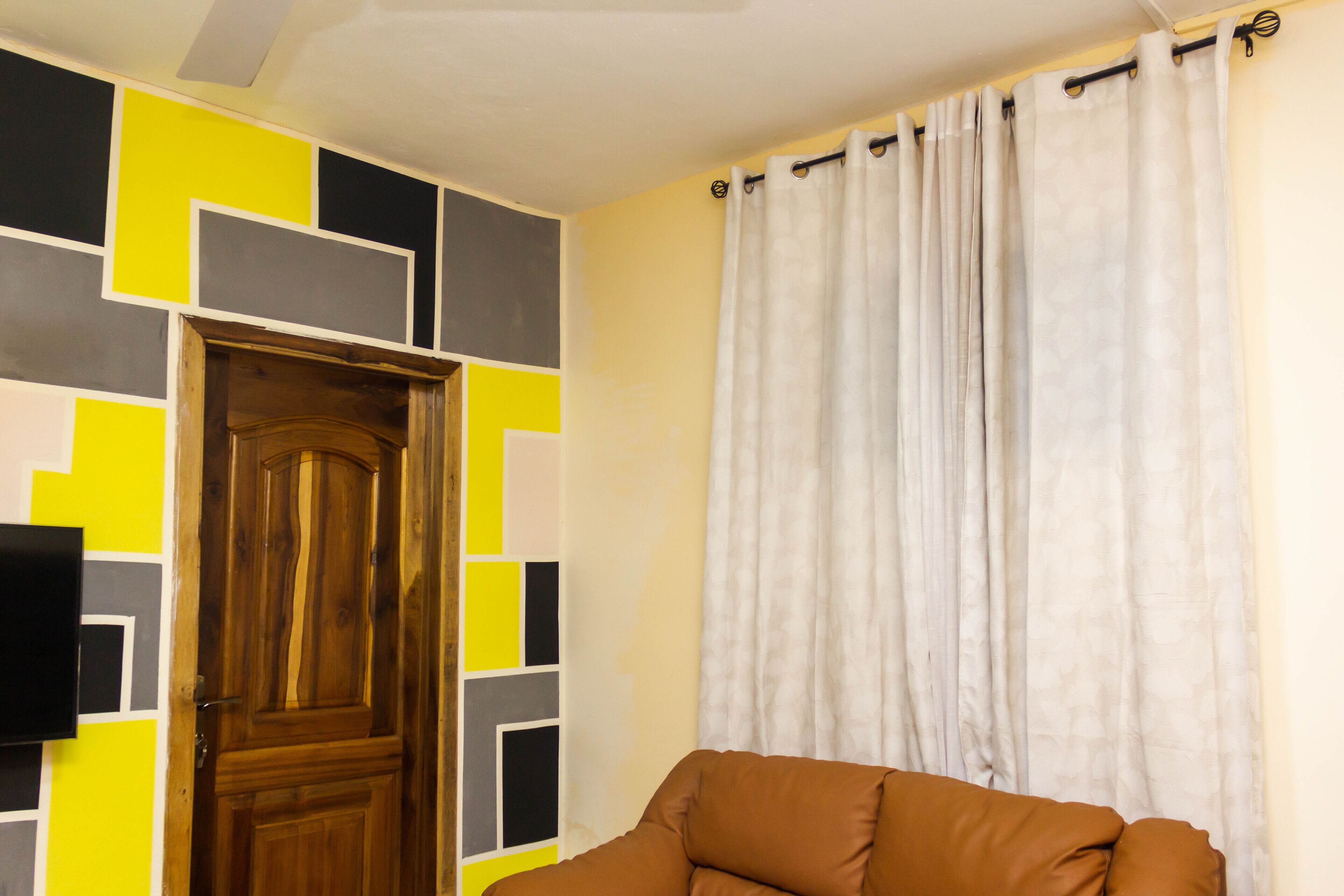 A room with a wooden door, a brown sofa, and a wall with geometric patterns.