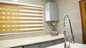Un baño con pared de mármol, una ventana con persianas, un lavamanos y un cabezal de ducha.