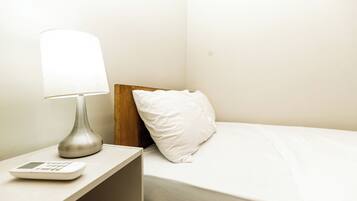 Una cama con un almohadón blanco, una mesita de noche con una lámpara y un pequeño dispositivo electrónico.
